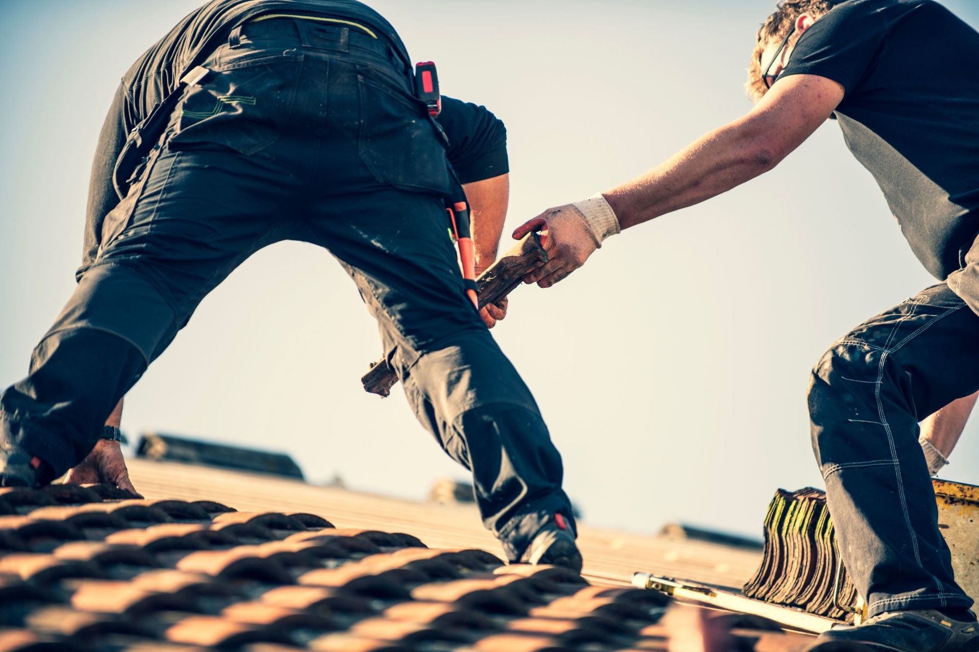 Handschutz im Sommer - Dachdecker verrichten ihre Arbeit auf einem Dach im Sonnenschein