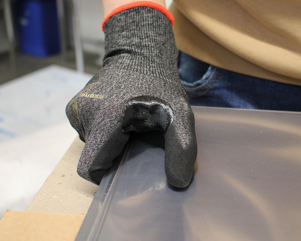Arbeiter nimmt ein Blech in die Hand und trägt dabei Arbeitshandschuhe zu seinem Schutz vor scharfen Kanten